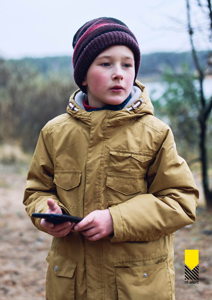 Jongetje in een natuurgebied met mobiele telefoon in zijn hand.