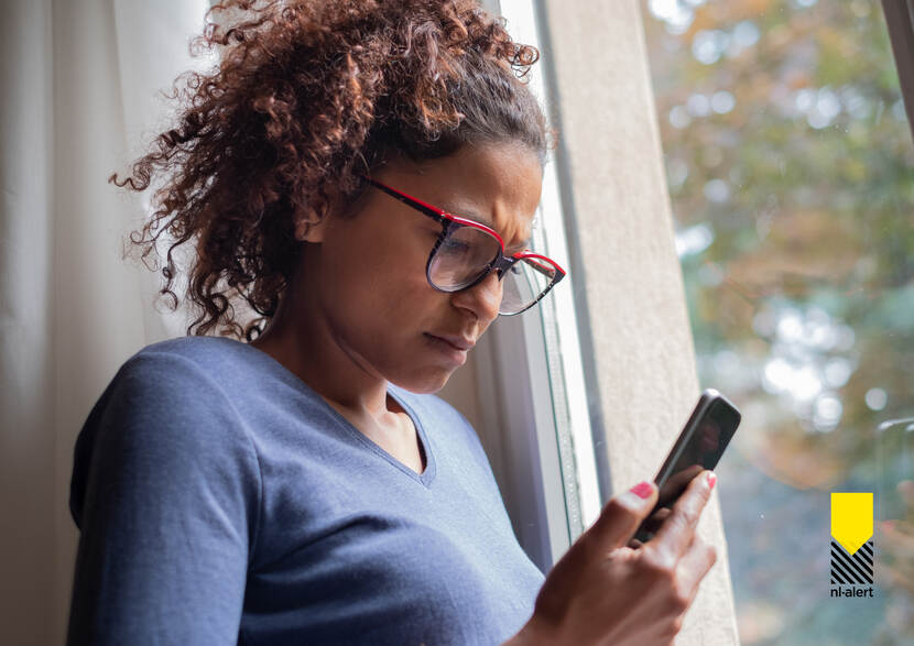 Vrouw kijkt op mobiele telefoon in haar hand.